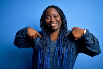 African american plus size woman with braids wearing casual sweater over blue background looking...