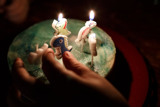 happy birthday cake with candles in the form of dinosaur figures with a child s hand on a dark background