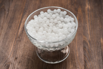 hydrogel white balls in glassware on wooden board. artificial moisture-absorbing material that contributes to accumulation and preservation of moisture. used for planting plants or children games