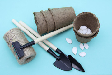 Garden tools: shovel, rake, peat pots isolated on a soft mint background. Seeds and home gardening....
