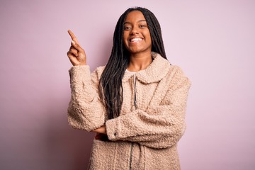 Young african american woman wearing fashion winter coat over pink isolated background with a big smile on face, pointing with hand and finger to the side looking at the camera.