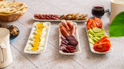 breakfast table: chopped vegetables, sliced meat, boiled eggs on long white porcelain plates on a white tablecloth