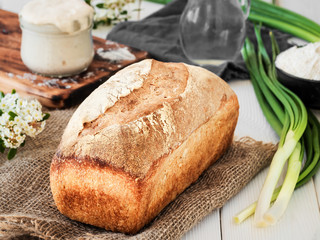 Freshly baked bread on burlap, sourdough and flour with a jug of water on a white wooden table. Hobbies, baking wheat bread at sourdough at home. Healthy food concept, traditional craft bread. Closeup
