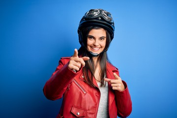 Young beautiful brunette motorcycliste woman wearing motorcycle helmet and jacket pointing fingers to camera with happy and funny face. Good energy and vibes.