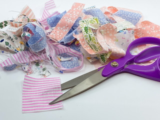 Close up view of a dressmaking scissors with a pile of scraps of printed patterned fabric