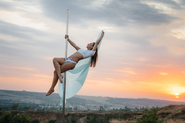 A young sexy girl performs amazing exercises on a pole during a beautiful sunset. Dance. Sexuality
