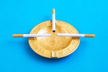 original golden ashtray with cigars resting on a blue background