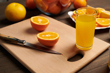 Fresh orange fruit whole and sliced on a wooden table, cutting board and kitchen knife. A plate full of citrus slices - natural and healthy food. Glass of fruit cocktail.