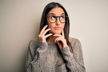 Young beautiful brunette woman wearing glasses having conversation talking on smartphone serious...