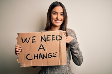 Young beautiful brunette activist woman protesting for a change holding banner with surprise face...