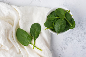 Green spinach leaves in a white bowl on a white table. View from above.