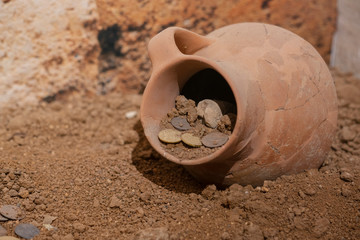 Antique coins in an ancient pottery jug. Old mesopotamia money. The treasure. Antique cracked amphora with poured out gold, ancient treasure artifact