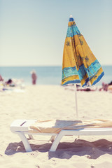 Summer vertical composition of a beach umbrella and deck chair with a carelessly thrown beach towel. Sun sand sea and beach
