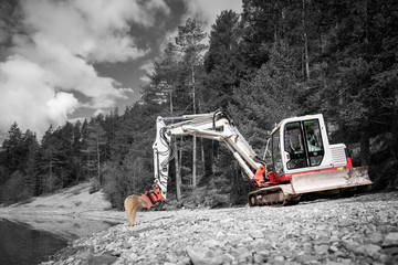 color key of small bucket excavator on gravel shore at lake and forest trees