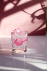 Glass with colored ice on a pink background with beautiful shadows.