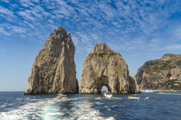 The Faraglioni rock formation off the coast of Capri. Small boats are approaching the arch.