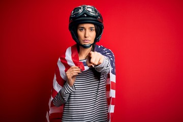 Young beautiful patriotic motorcyclist woman wearing moto helmet and united states flag pointing with finger to the camera and to you, hand sign, positive and confident gesture from the front