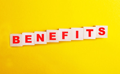 the word benefit on wooden cubes is red on a yellow background