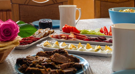breakfast table: chopped vegetables, sliced meat, boiled eggs on long white porcelain plates on a white tablecloth