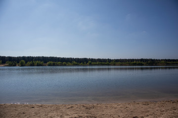 lake with beach and trees under blue sky background