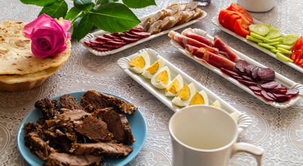 breakfast table: chopped vegetables, sliced meat, boiled eggs on long white porcelain plates on a white tablecloth