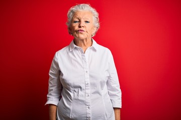 Senior beautiful woman wearing elegant shirt standing over isolated red background looking at the camera blowing a kiss on air being lovely and sexy. Love expression.