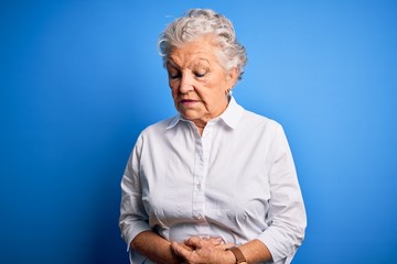 Senior beautiful woman wearing elegant shirt standing over isolated blue background with hand on stomach because indigestion, painful illness feeling unwell. Ache concept.