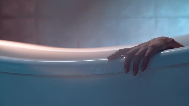 A woman is touching the edge of the white bathtub elegantly