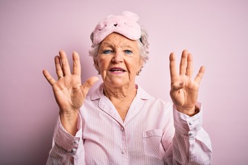 Senior beautiful woman wearing sleep mask and pajama over isolated pink background showing and pointing up with fingers number nine while smiling confident and happy.