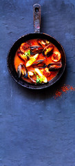 Fototapeta na wymiar Mussels in red curry sauce in a cast iron pan on blue background. Calming Simplicity and Sustainable health for quarantine. Close-up