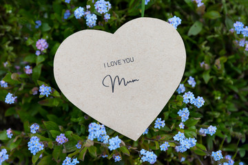 I love you mum written on a heart-shaped card on forget-me-nots and grass