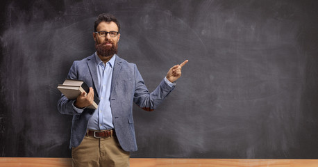 Fototapeta Male teacher holding books and pointing at a chalkboard obraz