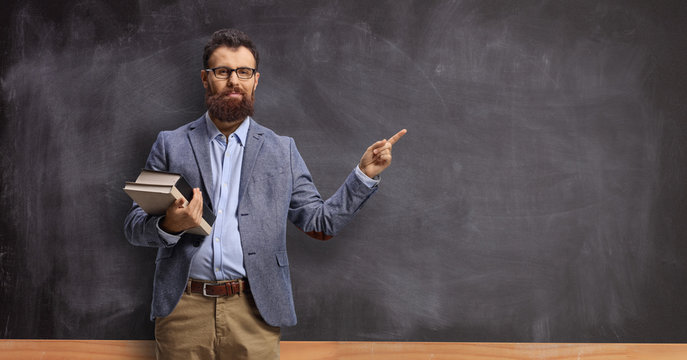 Male teacher holding books and pointing at a chalkboard