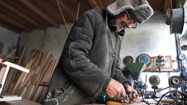 Grandfather in old clothes fastens the borer to the drill