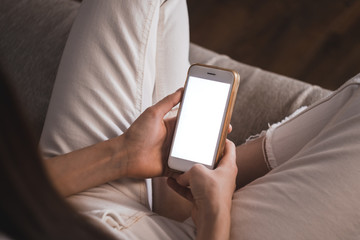Woman uses a smartphone with a white screen, sitting at home on a sofa in the evening. Mock up