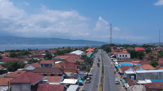 flying on a drone over a road with cars in sunny weather in the background the sea and mountains are not front red roofs of houses Gilimanuk Melaya west bali indonesia