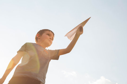 Little boy launches a paper plane into the air. Child launches a paper plane. Happy kid playing with paper airplane