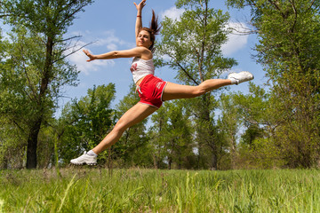 Young athletic girl doing an acrobatic stunt in the air. Jump Twine. Doing sport outside