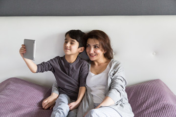 Mother and son having happy family time at home watching a movie on tablet, cozy family time concept