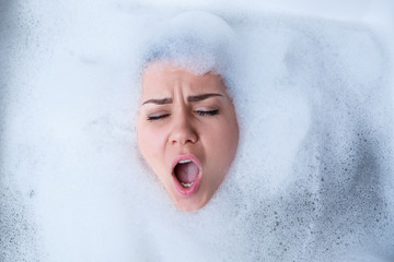 Closeup portrait of a girl in a bathtub and white foam around her face. Different emotions, grimaces, woman smile