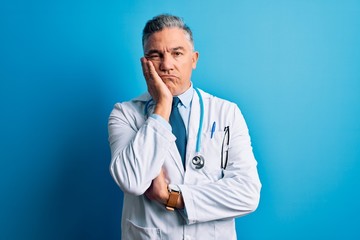 Middle age handsome grey-haired doctor man wearing coat and blue stethoscope thinking looking tired and bored with depression problems with crossed arms.