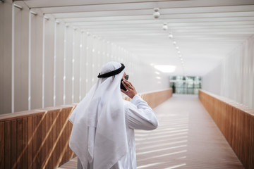 Emirati guy taking selfie in the urban city lifestyle downtown the heart of Dubai. Arabic guy wearing kandura taking site visit for expo 2020 with investor negotiating over the phone