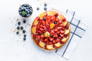 Homemade open tart with strawberries, raspberries, blueberries and grapes on a grey background. Homemade cake. The concept of healthy and delicious food. Top view, copy space.