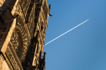 Fototapeta na wymiar Historic monument, a cathedral in Gothic architecture, with the contrail of an airplane against the background of a blue sky