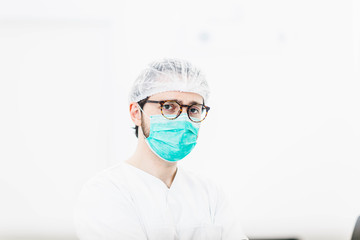 Naklejka premium male surgeon doctor in uniform and medical mask stands in a bright clinic office.