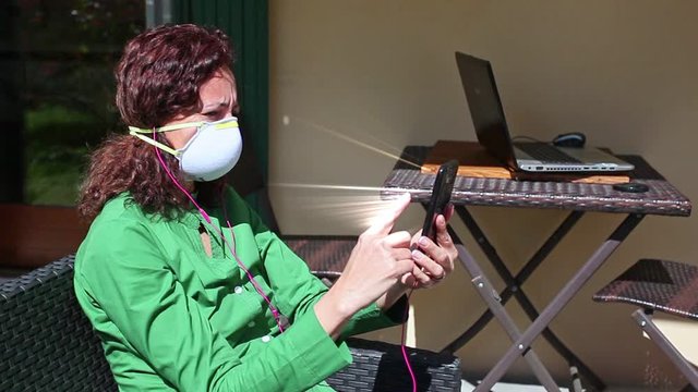 Futuristic effect of woman sitting in the garden, wearing an anti-covid mask, while using her phone to search for news. Concept: actions at home during coronavirus quarantine