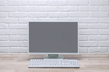 Blank screen computer monitor on working desk with brick wall