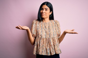 Young beautiful hispanic fashion woman wearing elegant style over pink background clueless and...