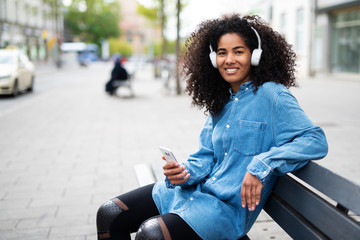 Portrait einer lachenden jungen Frau mit Kopfhörern in der Stadt 