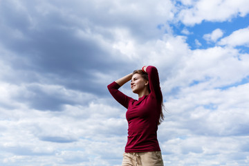 Joyful young girl on a background of the sky with clouds. He raised his hands up and laughed. Happiness in lifestyle. Inspiration in nature. Rest after a good working day.